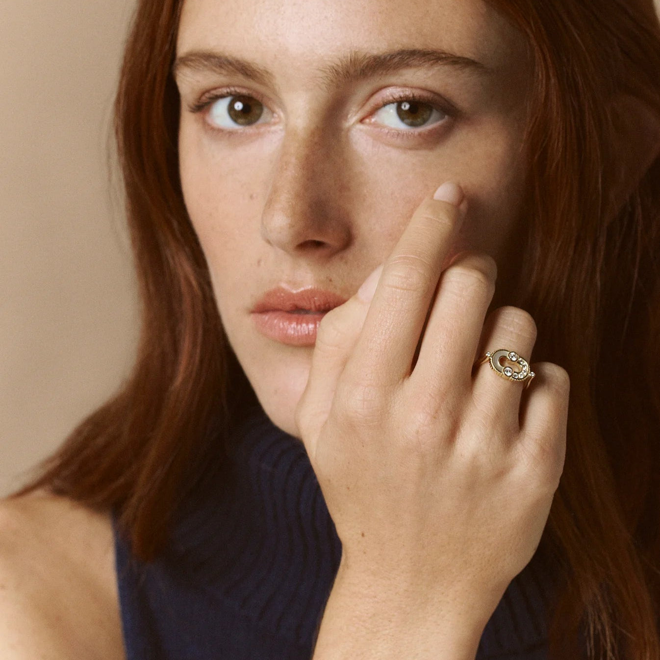 Woman with red hair wearing a dark blue sleeveless top against a beige background