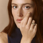 Woman with red hair wearing a dark blue sleeveless top against a beige background